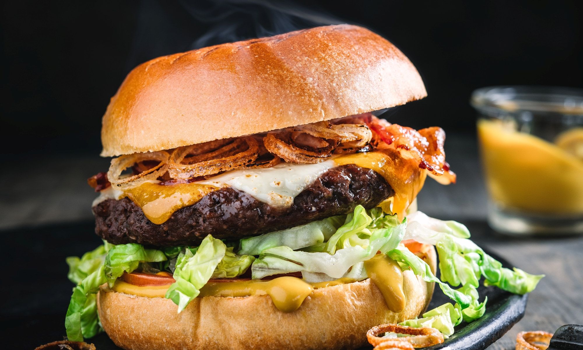 En saftig hamburger med ost, salat og bacon i et brød, med en liten skål med saus ved siden av.