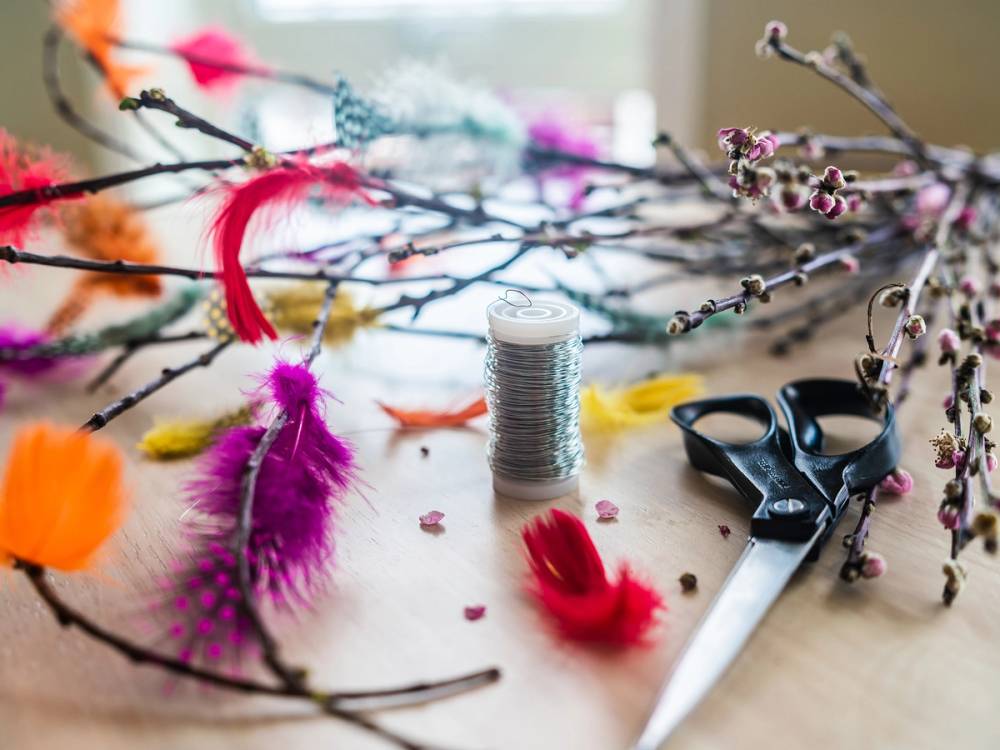 Bilde av bjørkeris med pynt, tråd, saks og fjær, brukt til fastelavn-dekorasjon.