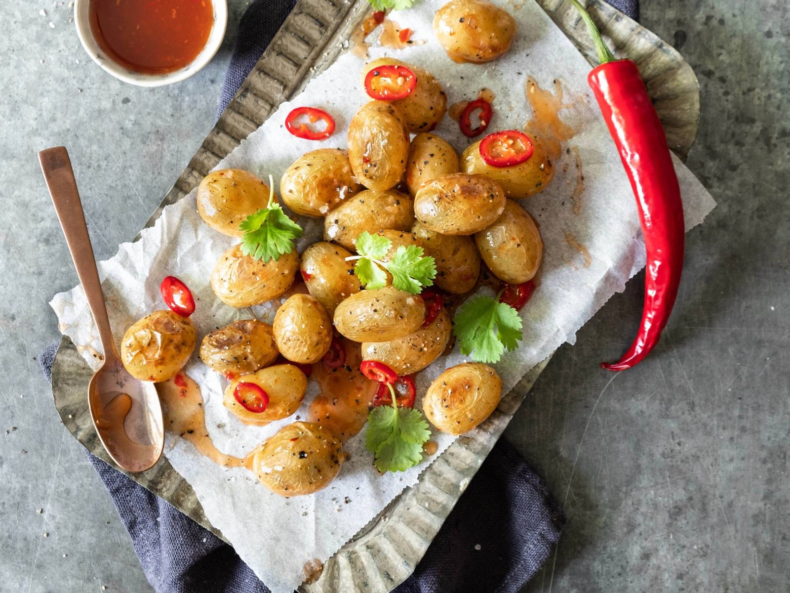 Små, ovnsbakte poteter med chili og frisk koriander på et serveringsfat med en skje ved siden av.