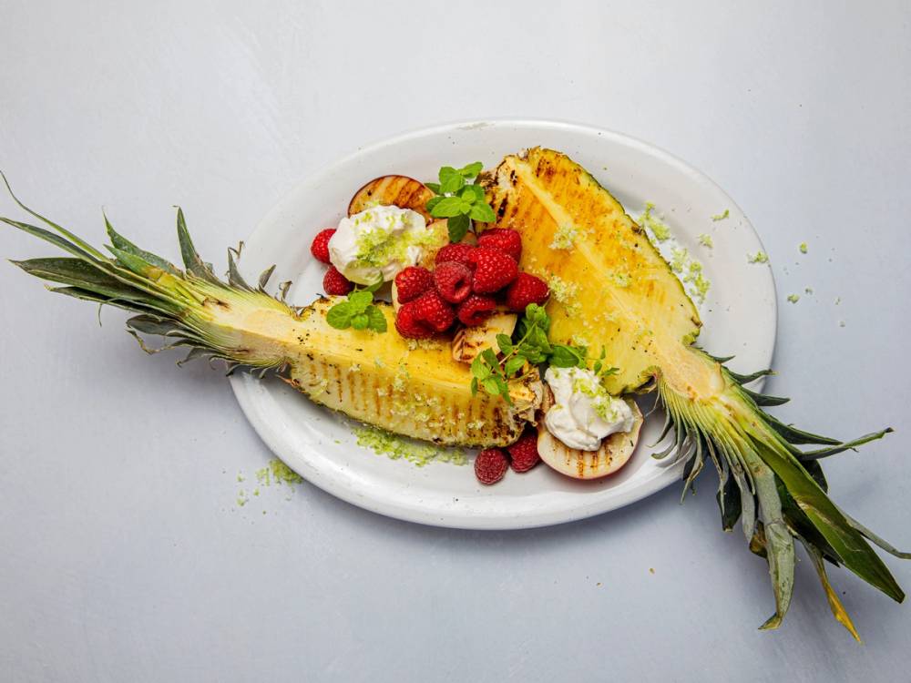 Ananas og jordbær som er grillet og servert på en tallerken med litt grønt til pynt.