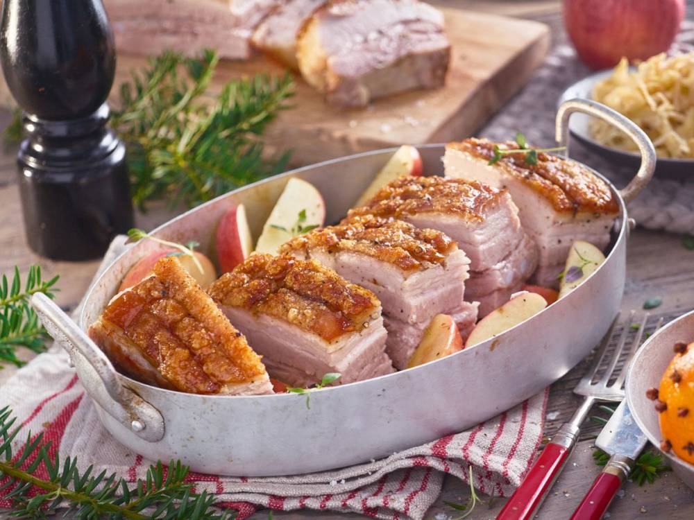 Ribbe med sprø svor og skiver av eple på et fat, omgitt av julepynt og tilbehør.