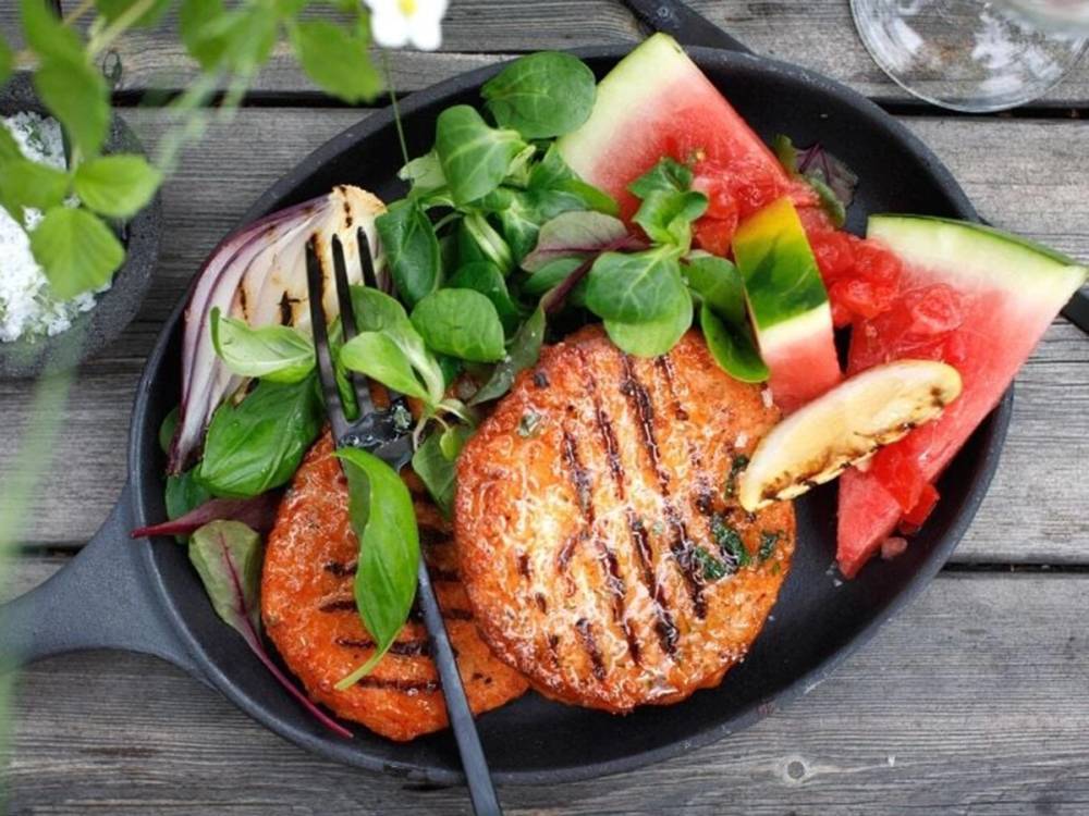 Storfjordørret servert med grønnsaker og vannmelon på en svart tallerken, plassert på et trebord.