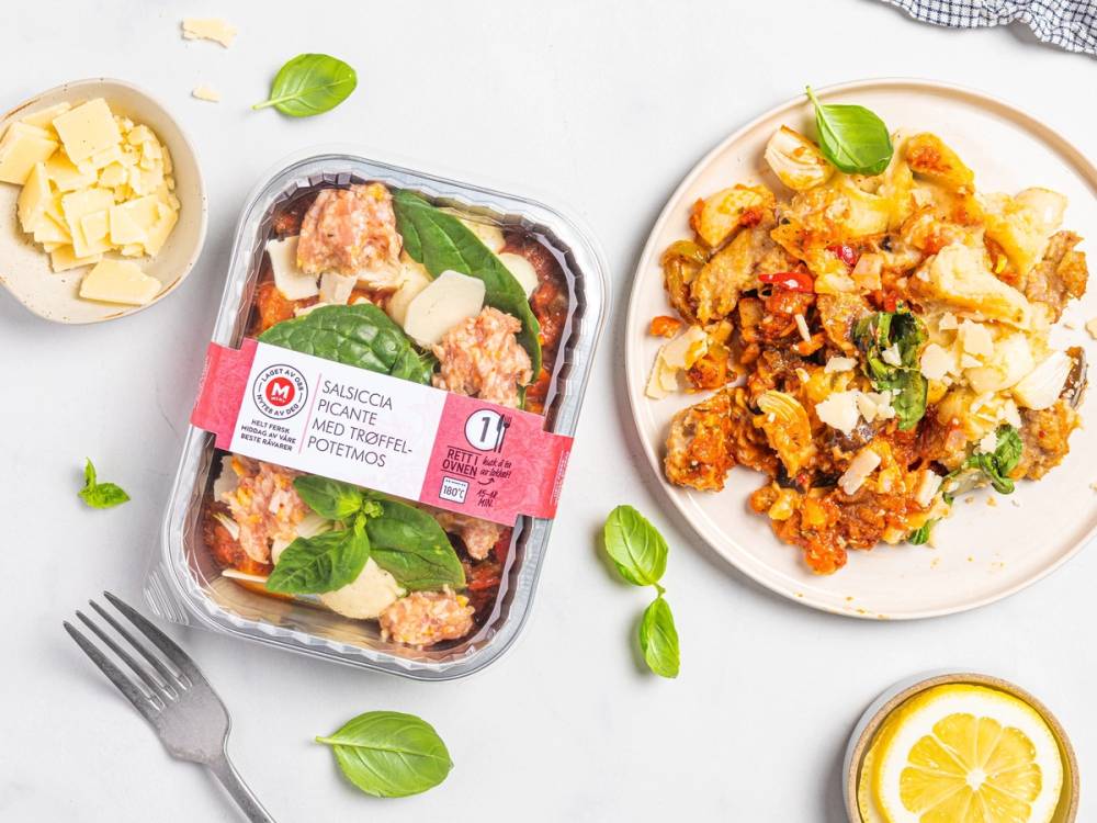 Salsiccia Picante med trøffel på en hvit tallerken, omgitt av ferske basilikumblader og sitronbiter, med en pakke av ferdigmat i bakgrunnen.