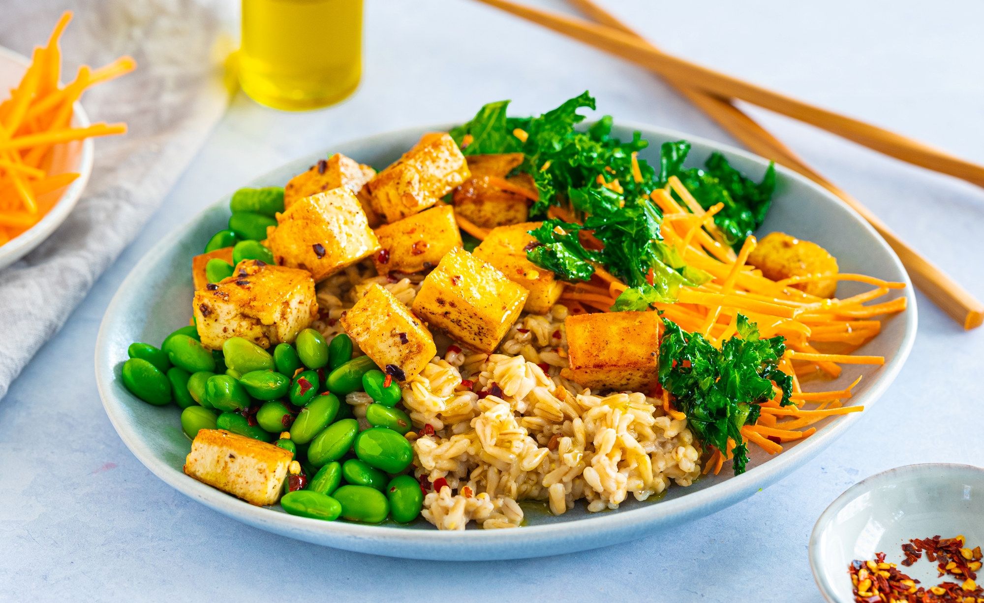 En tallerken med tofusalat med havreris, tofu i terninger, grønne erter, revet gulrot og frisk persille, med spisepinner ved siden av.