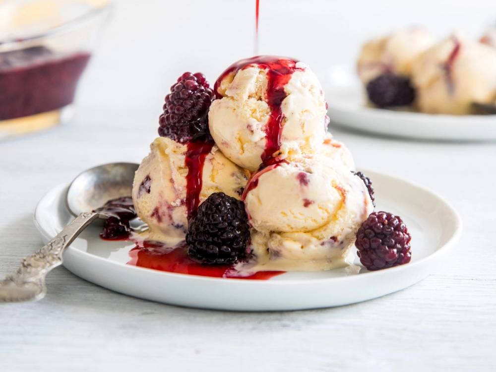 Iskrem med bringebærsaus og friske bringebær på en hvit tallerken, med en skje ved siden av.