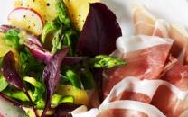 Tallerken med skiver av spekeskinke og en frisk salat med grønnsaker og urter.