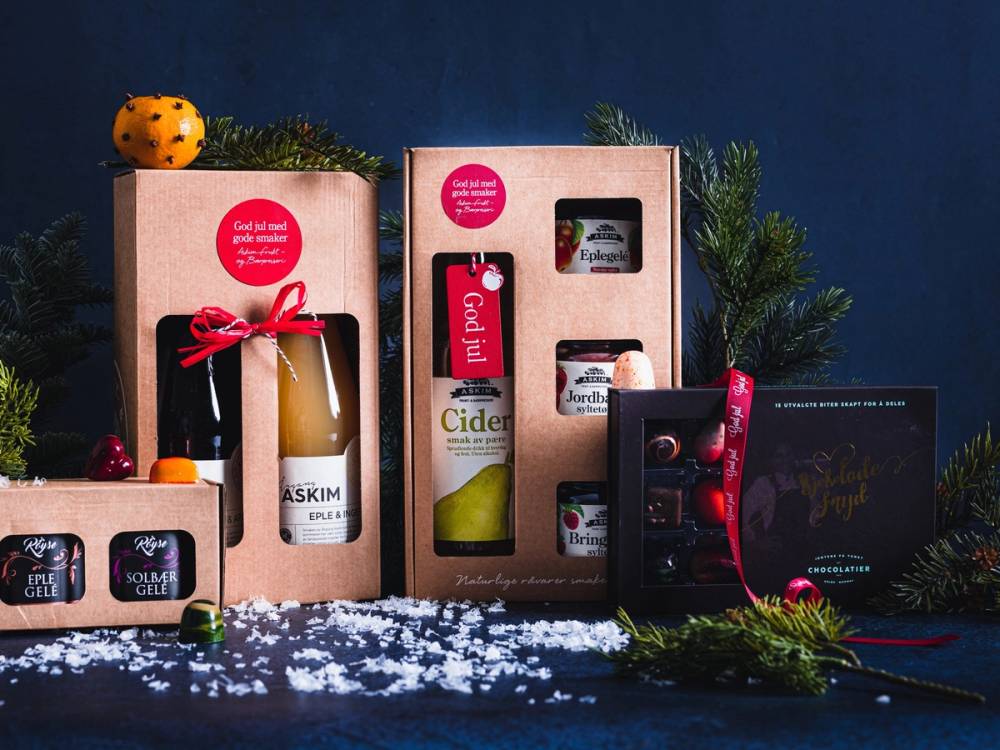 Ulike gave esker med julepynt og produkter, dekorert med granbar og snø, mot en mørk bakgrunn.