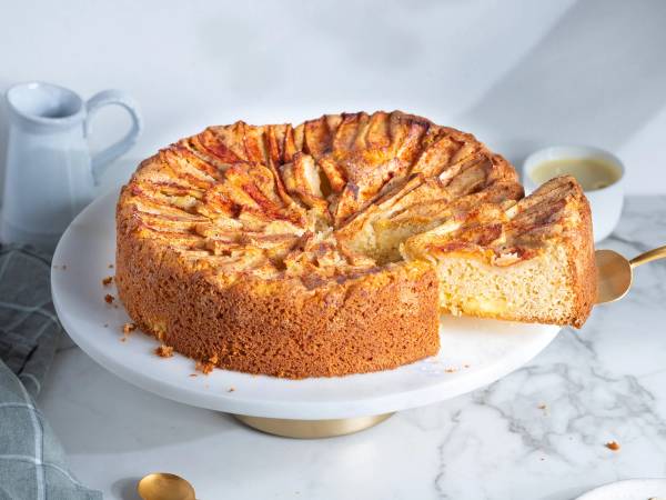 Eplekake med vaniljekrem på en hvit tallerken, med en skje ved siden av.