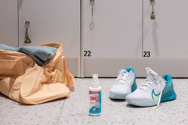 Et par hvite og blå treningssko plassert på gulvet foran en dør, med en sprayflaske og en pose ved siden av.