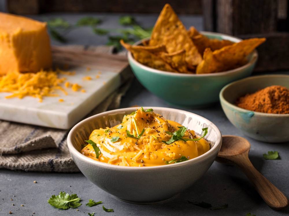 Cheddarsaus i en skål med tortilla chips og krydder i små skåler på et bord.