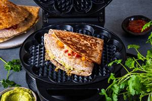 En tortilla wrap delt i to, fylt med grønnsaker og saus, plassert på en svart tallerken med urter og en liten skål med saus i bakgrunnen.