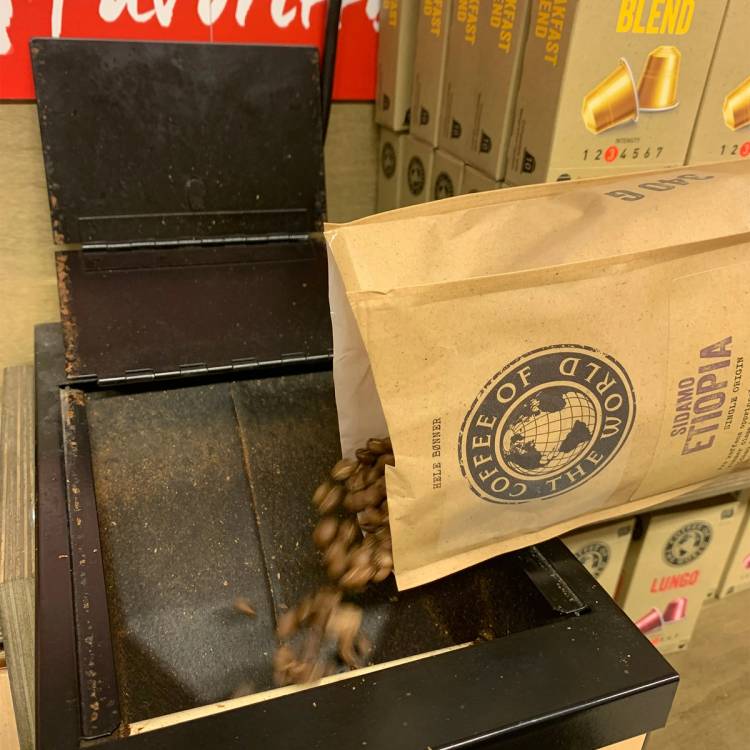 Kaffekvern med kaffebønner som faller ned i en eske, plassert i en butikkhyller.