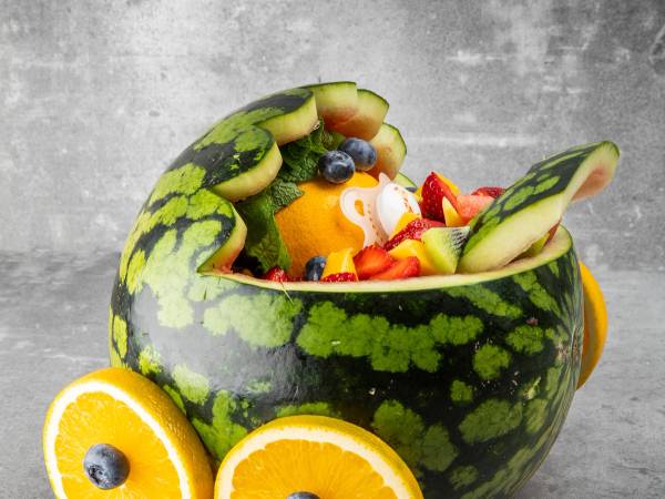 En vannmelon som er fylt med frukt og pynt, med skiver av vannmelon rundt og en blåbær på toppen.