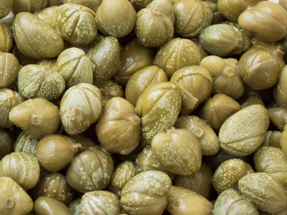 Nærbilde av kapers med små, runde, grønne og beige farger, noen med hvite striper eller prikker.