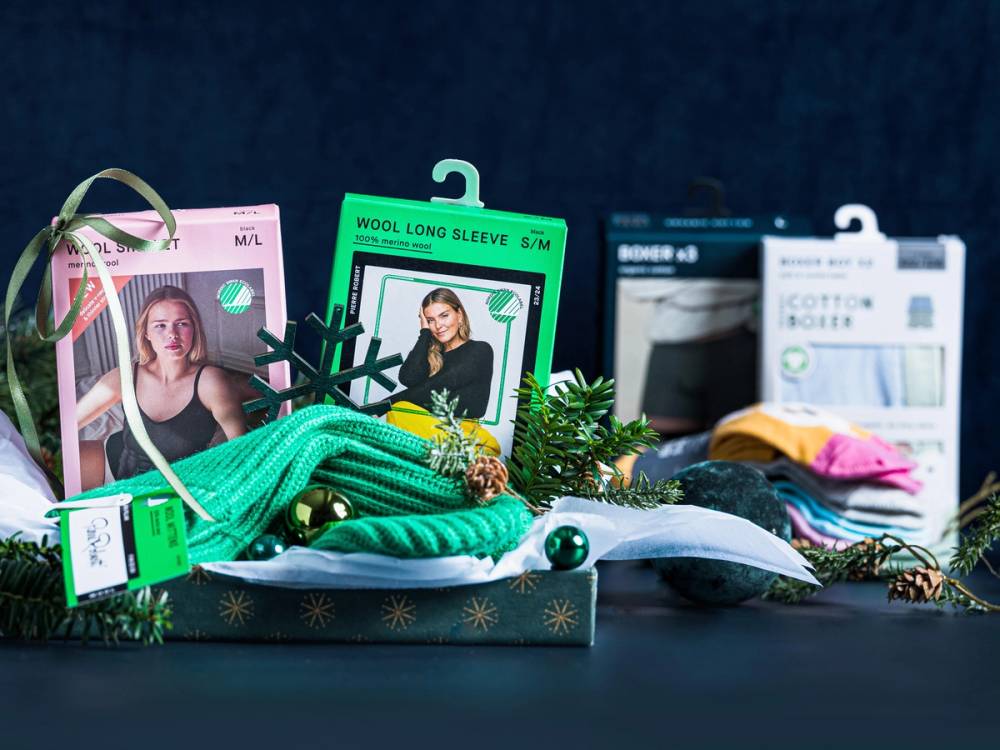 Ulike ullgaver og garnpakker på et bord, inkludert strikkepinner og julepynt, med en pakke som har bilde av en person på etiketten.