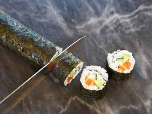 Sushiruller med laks, agurk og kremost, og en kniv som skjærer i en av rullene