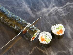 Sushiruller med laks, agurk og kremost, og en kniv som skjærer i en av rullene