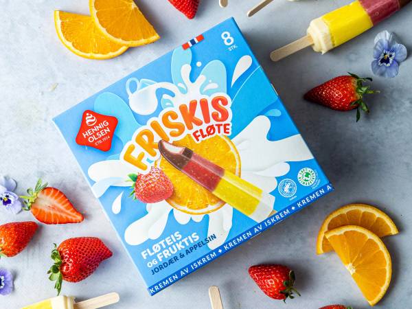 En pakke med Hennig-Olsen Friskis Fløte iskrem omgitt av jordbær og appelsinskiver på en grå bakgrunn.