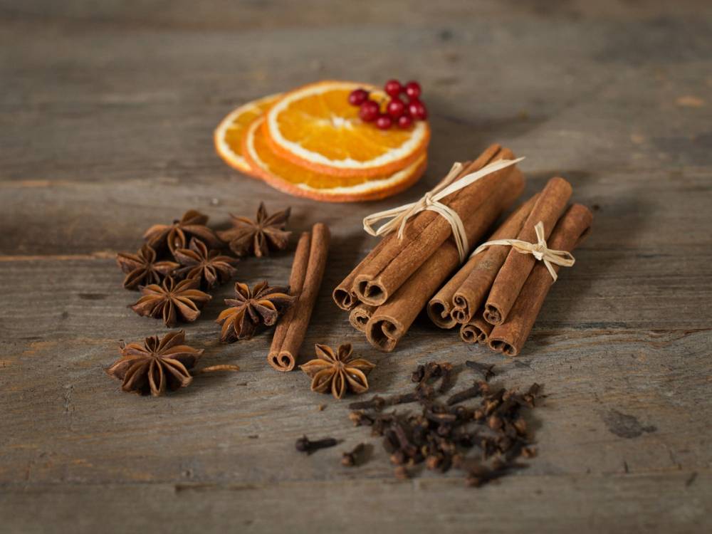 Kanelstenger, stjerneanis, appelsinskiver og nellik ligger på et trebord, brukt til julebakst og pynting.