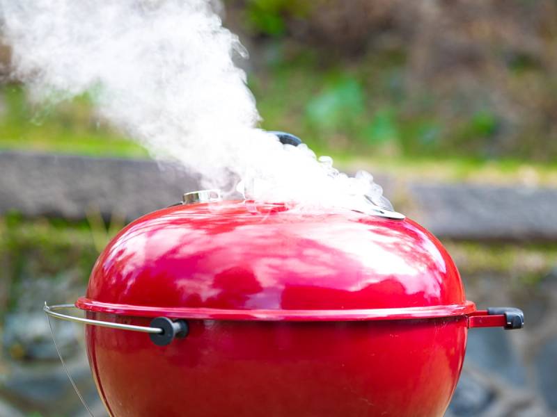 En rød kullgrill med damp som stiger opp, sannsynligvis brukt til grilling av sjømat eller skalldyr.