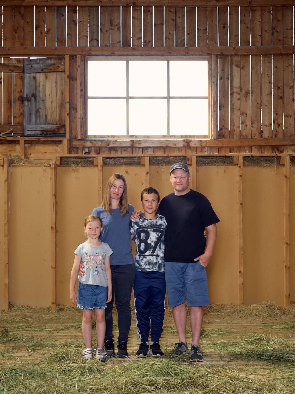 Fire personer står inne i en trebygning med uferdig vegg og et stort vindu bak dem.