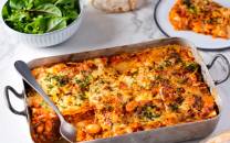 Vegetarisk lasagne i en ildfast form med ost og grønnsaker på toppen, med en skje i formen og en salat ved siden av.