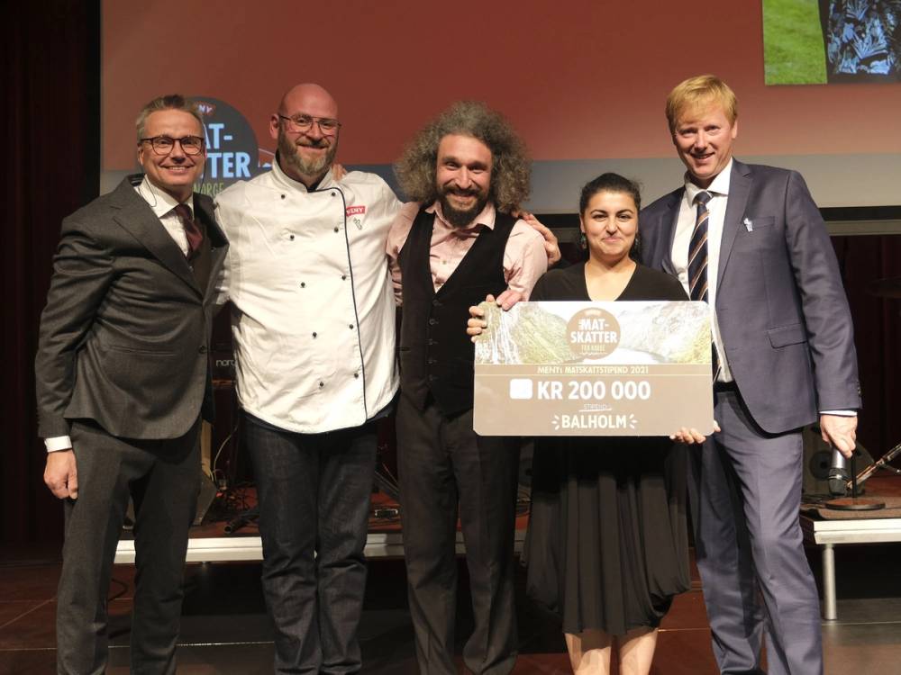 Fem personer står på scenen og holder et stort sjekk for Matskattstipendet 2021, med en presentasjon i bakgrunnen.