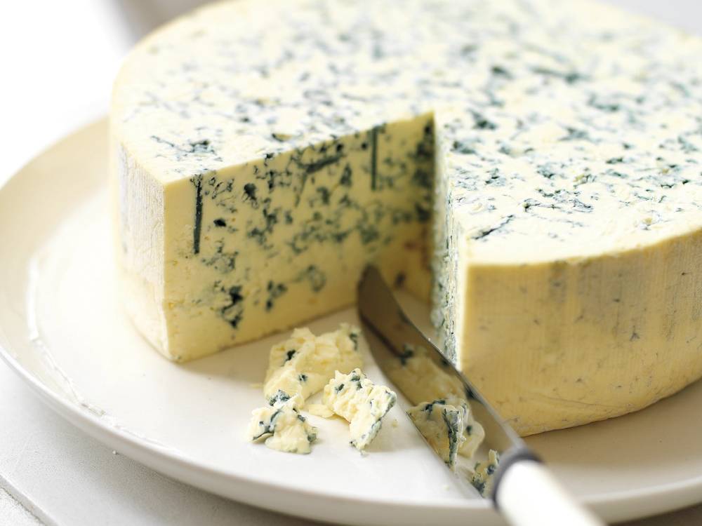 Blåmuggost med blå og hvite muggflekker på en hvit tallerken, med en kniv som skjærer i osten.