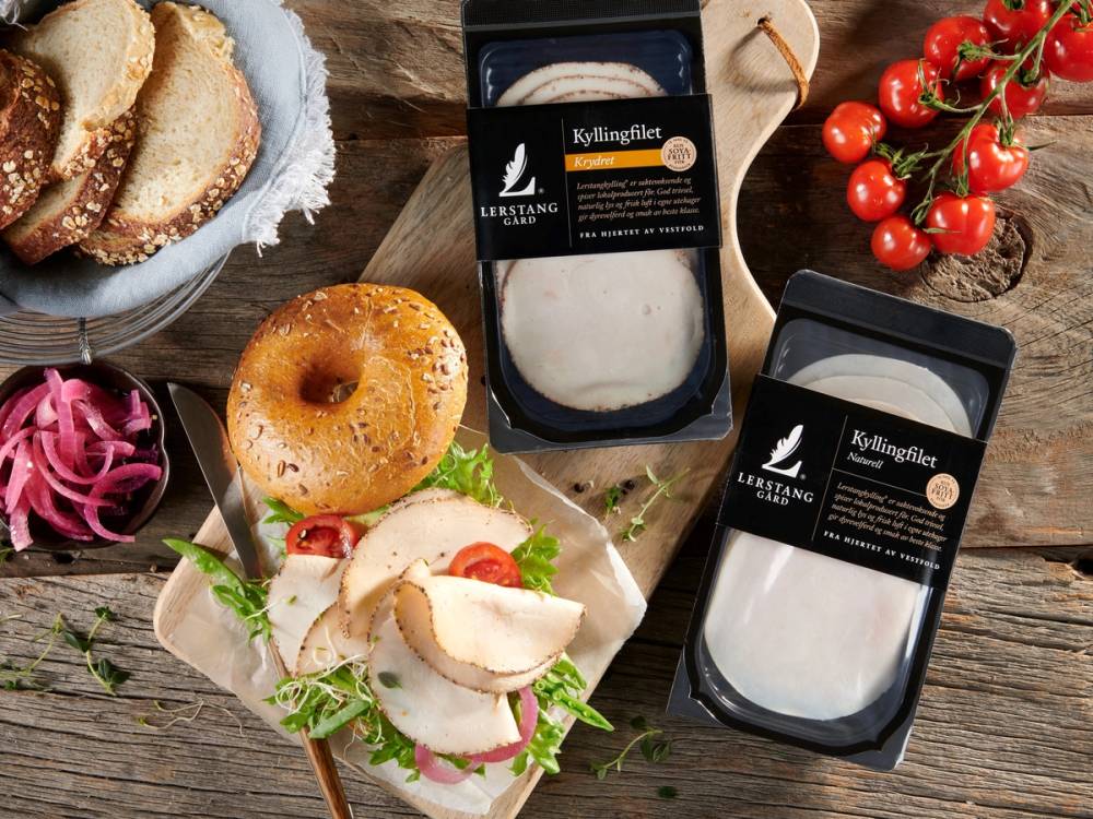 Kjøtt- og grønnsaksfat med bagels og to pakker med kyllingfilet på et tre- eller trebord, omgitt av cherrytomater og rødløk, på bildet 20210208 Lerstang Miljøbilder 02.jpg