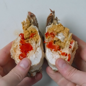 To personer holder et krabbehus som er delt i to, med innhold av krabbe og majones, i hendene sine.