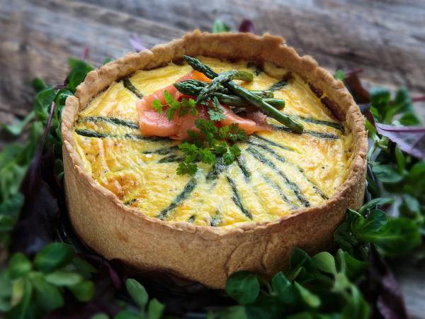 En pai med en gul eggerøre-fylling pyntet med grønne urter og grønnsaker, omgitt av grønne blader.