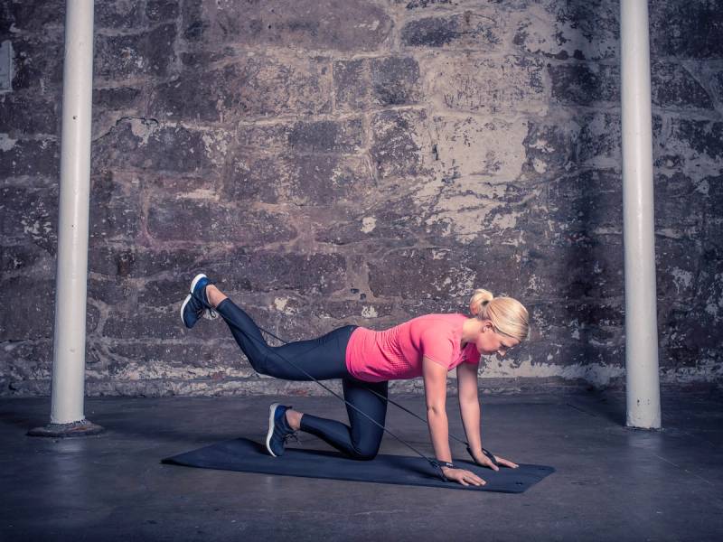 En kvinne gjør en øvelse på gulvet i et treningsrom med en murvegg i bakgrunnen.