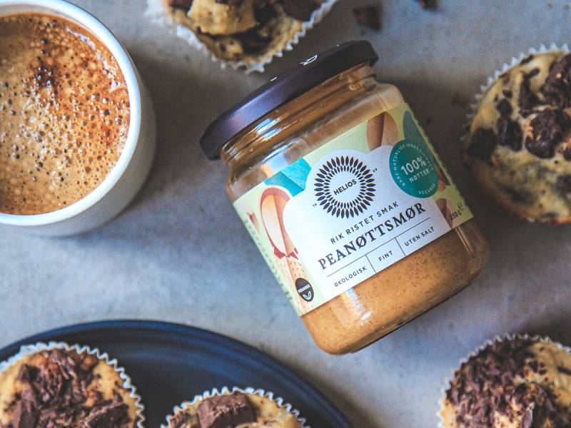Bananmuffins med peanøttsmør på en tallerken, med en glass med peanøttsmør i bakgrunnen.