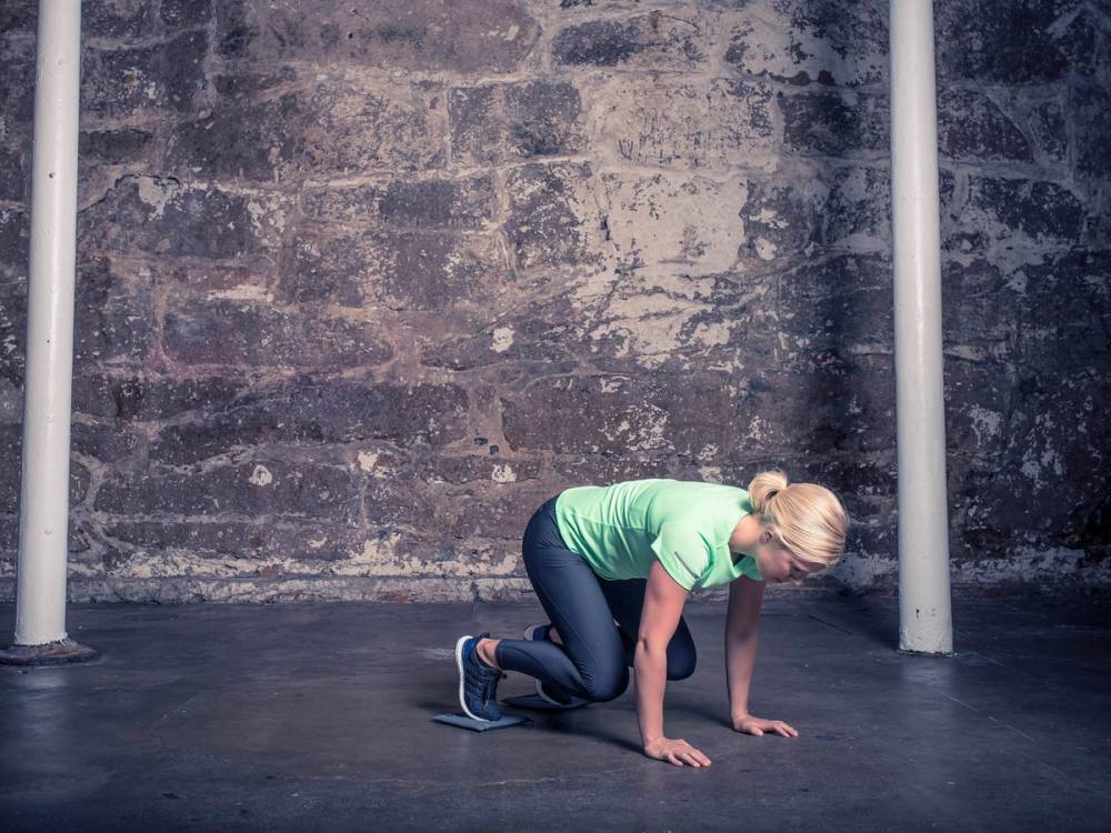 En kvinne i treningsklær på gulvet under en økt, med en murvegg i bakgrunnen.