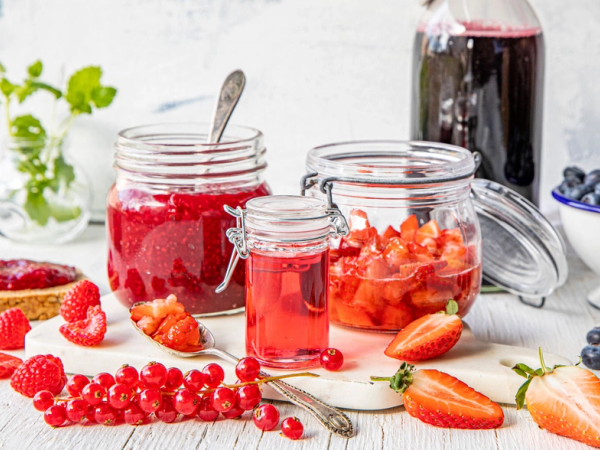 Et utvalg av friske bær, inkludert jordbær, bringebær, blåbær og rips, med en flaske og glass med bærjuice på et kjøkkenbord.
