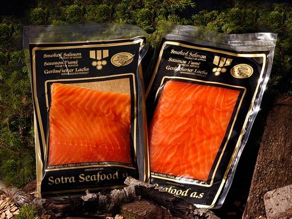 To pakker med Sotra-røykelaks plassert på en stein med grønt gress i bakgrunnen.