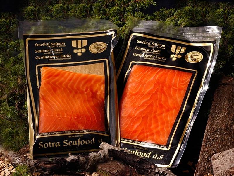 To pakker med Sotra-røykelaks plassert på en stein med grønt gress i bakgrunnen.