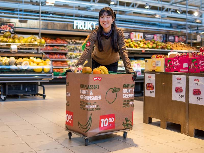 Kvinne med ansiktsmaske handler i en matbutikk med en handlevogn full av frukt og grønnsaker.