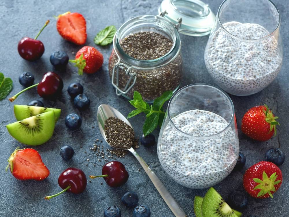 Ferske bær og chiafrø i glass og på en mørk overflate, med en skje og noen mynteblader