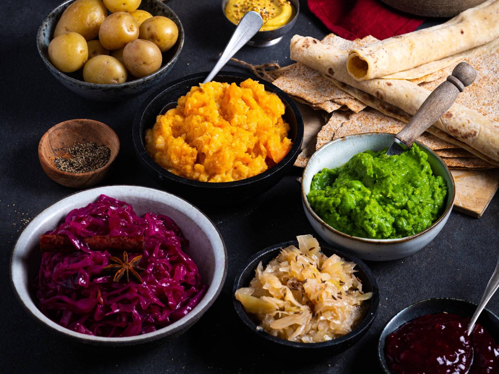 Ulike jule-tilbehør som poteter, rødkål, surkål, grønnsaker og saus på et bord.