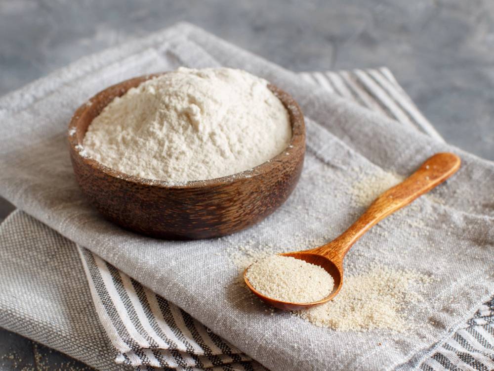 Glutenfritt mel i en treskål med en liten tresleiv ved siden av på et kjøkkenbord.