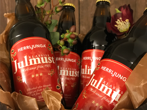 Flere flasker med svensk julebrus og julemat på bordet, dekorert med blomster og granbar.