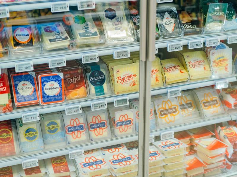 Frysedisplay med meieriprodukter i en butikk, med Tine-merker og ulike ostetyper synlige.