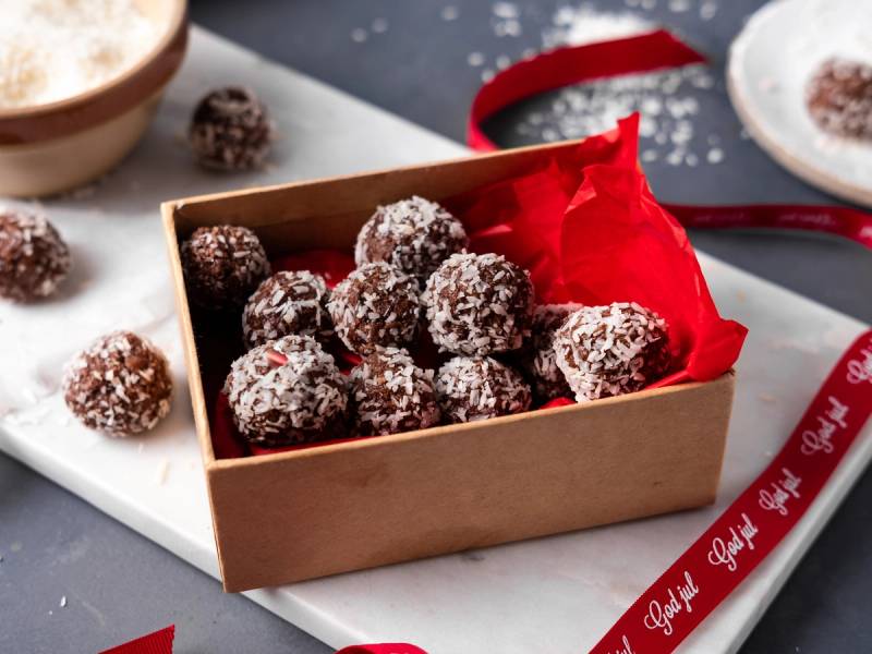 Bountyboller i en liten eske med rødt papir, omgitt av julepynt og gavebånd.