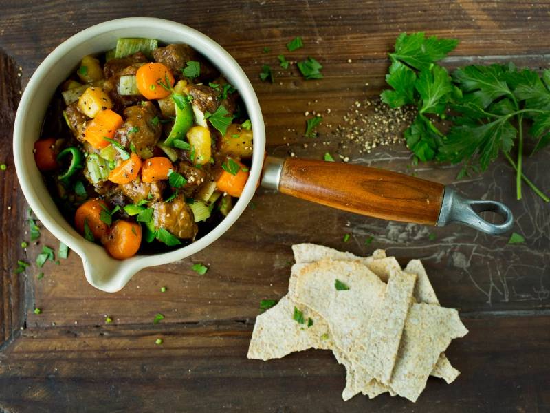 Lapskaus i en hvit bolle med brød og grønn urter på en treplate