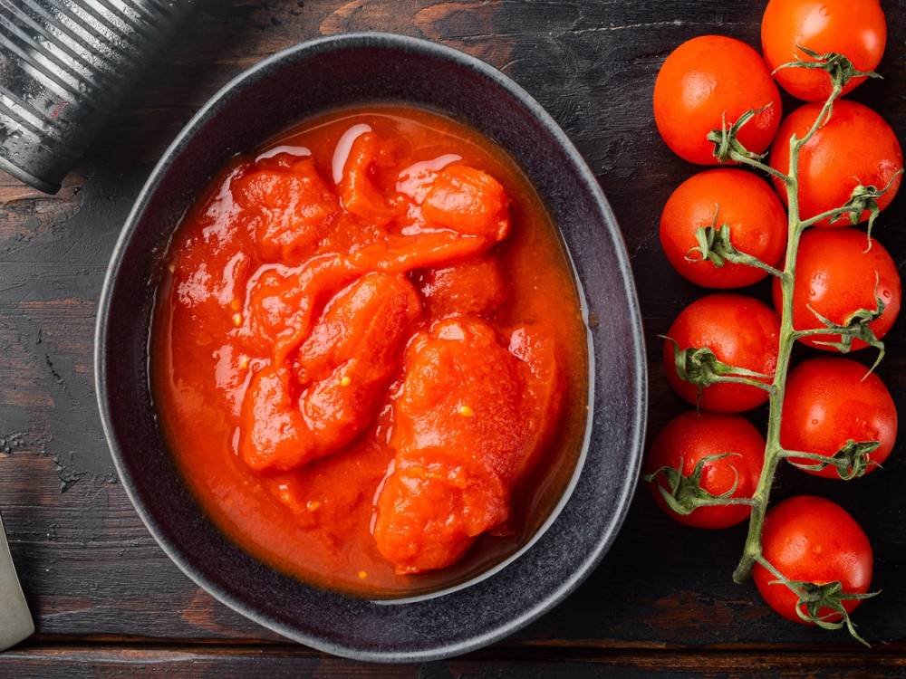 Tomater i saus på en svart tallerken med en klase ferske tomater på en gren ved siden av