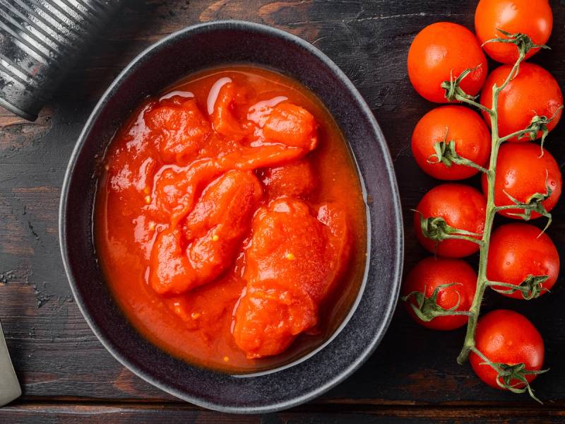 Tomater i saus på en svart tallerken med en klase ferske tomater på en gren ved siden av