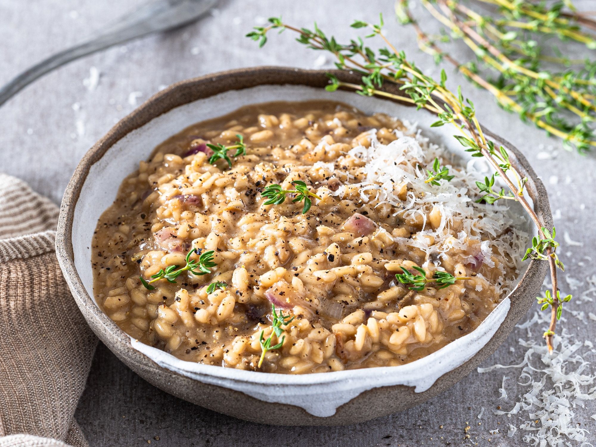 Risotto med steinsopp, pyntet med urter og revet ost i en grå skål på et bord.