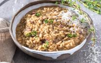 Risotto med steinsopp, pyntet med urter og revet ost i en grå skål på et bord.