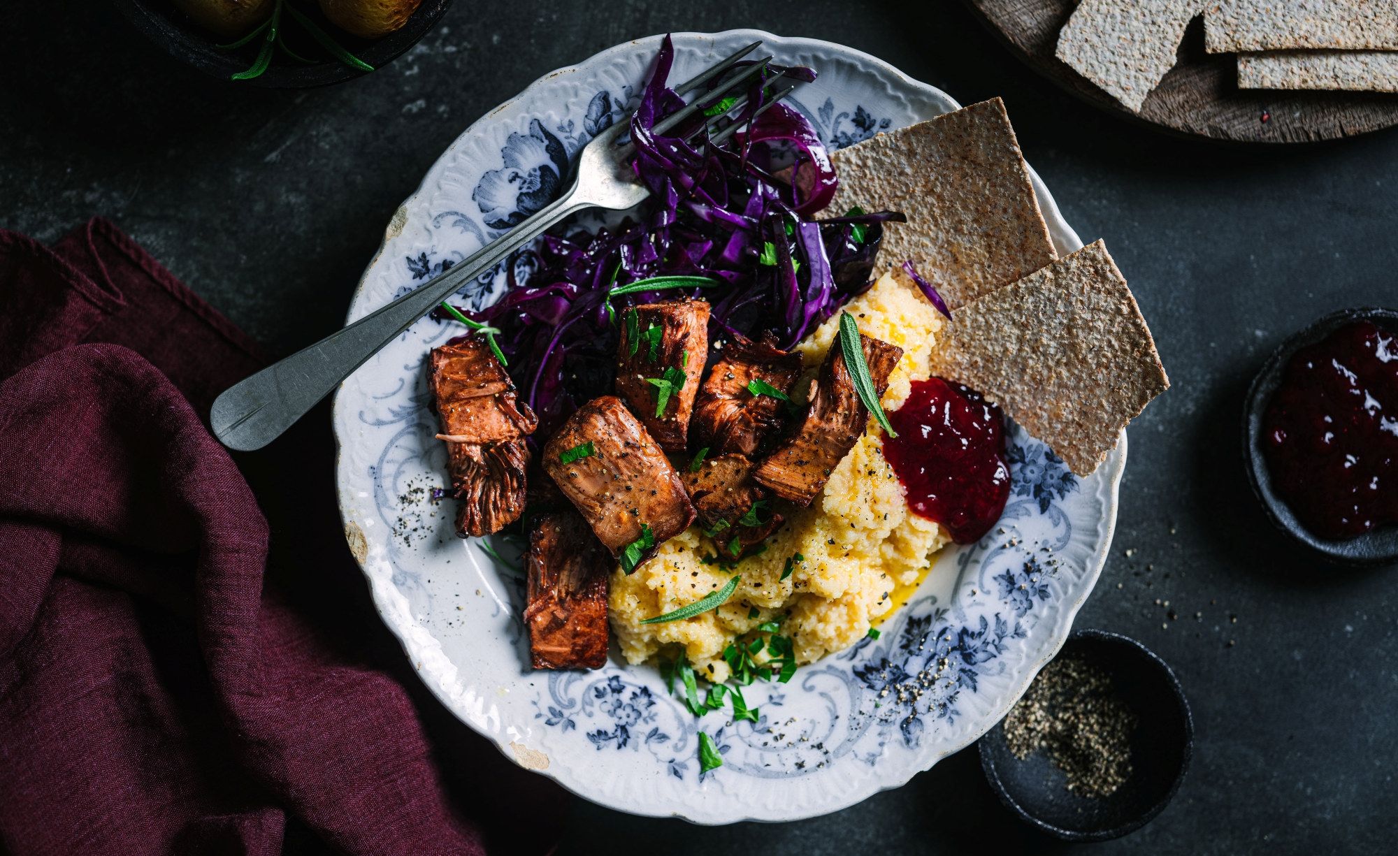 Vegetarisk pinnekjøtt laget av jackfruit servert med kålrotstappe og flatbrød på en blå og hvit tallerken.